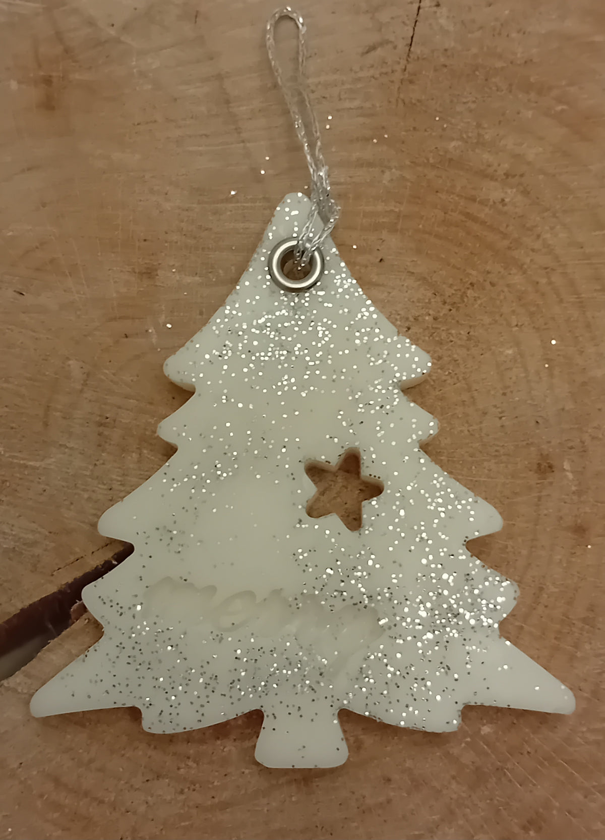 Christmas tree shaped wax sachet decorated with silver glitter on a wooden log slice background.